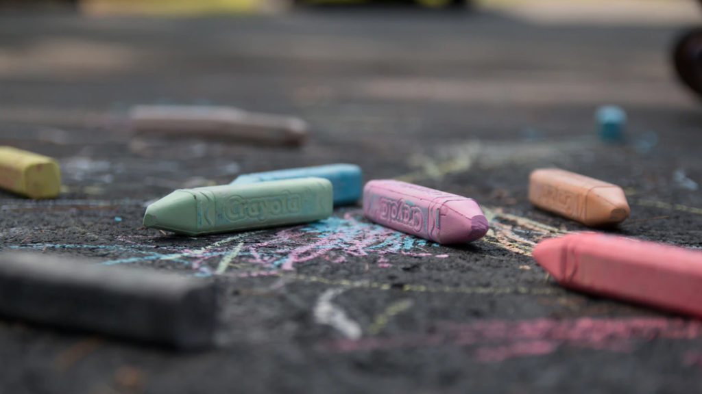 pieces of multi-color chalk laying on a sidewalk atop some chalk doodles