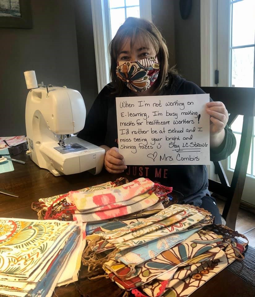 Lake Central High School Business Education teacher Dawn Combis sits by sewing machine with many homemade face masks, wearing one.